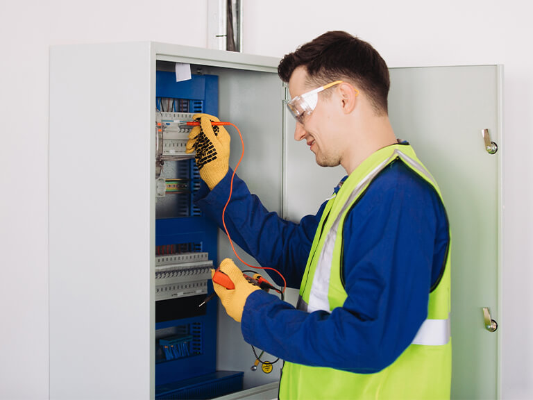 industrial electrician testing circuit breaker panel with multimeter