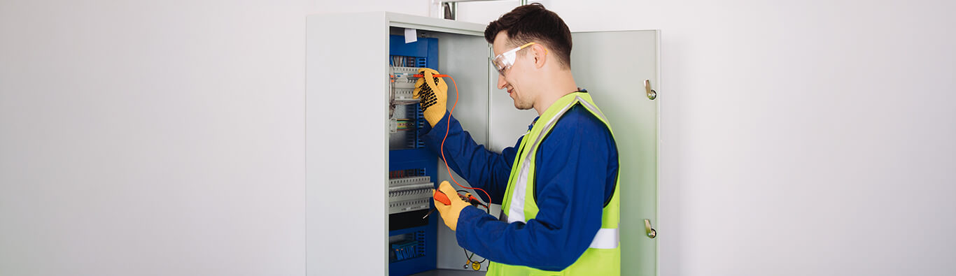 industrial electrician testing circuit breaker panel with multimeter